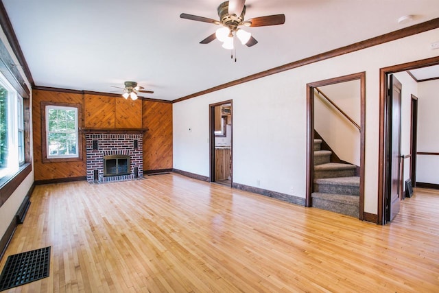 unfurnished living room featuring a brick fireplace, light wood-type flooring, ornamental molding, and wood walls