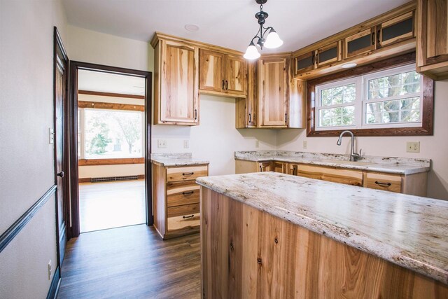 kitchen with dark wood-type flooring, light stone countertops, sink, and hanging light fixtures