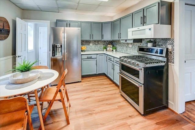 kitchen with appliances with stainless steel finishes, decorative backsplash, a drop ceiling, and light hardwood / wood-style flooring