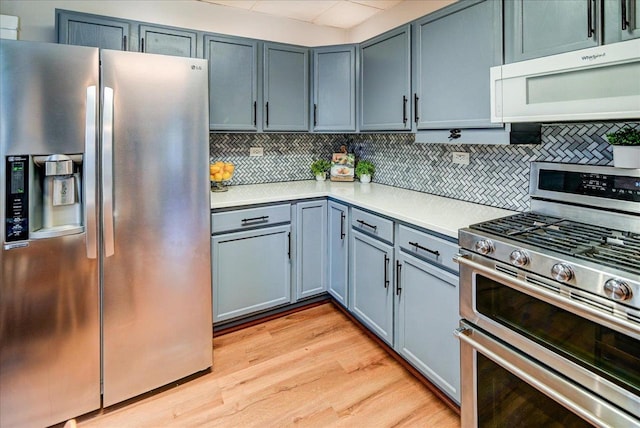 kitchen with appliances with stainless steel finishes, backsplash, and light wood-type flooring