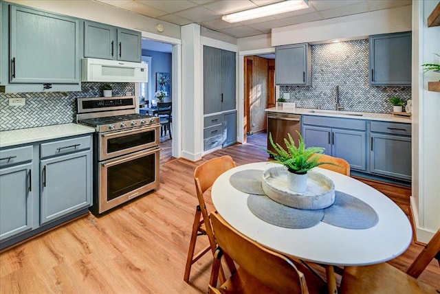 kitchen with appliances with stainless steel finishes, light hardwood / wood-style floors, backsplash, a drop ceiling, and sink