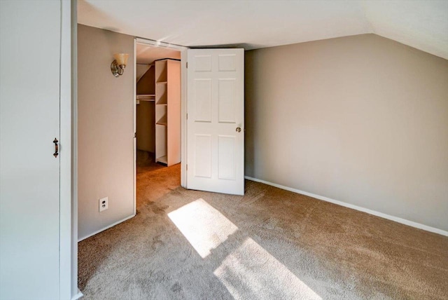 unfurnished bedroom with a walk in closet, vaulted ceiling, a closet, and light colored carpet