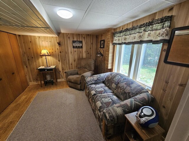 living room featuring a paneled ceiling, wooden walls, and hardwood / wood-style floors