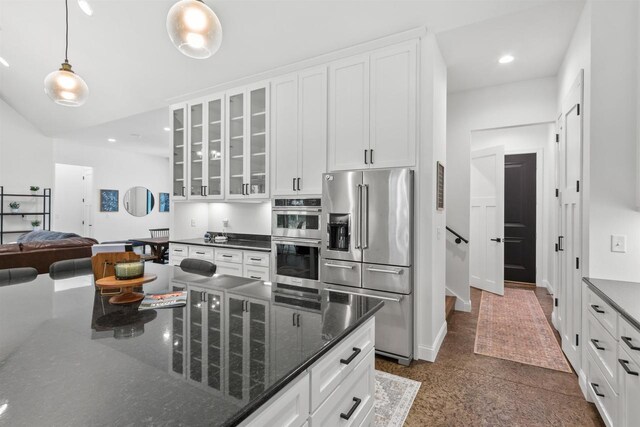 kitchen with white cabinetry, decorative light fixtures, stainless steel appliances, and dark stone counters