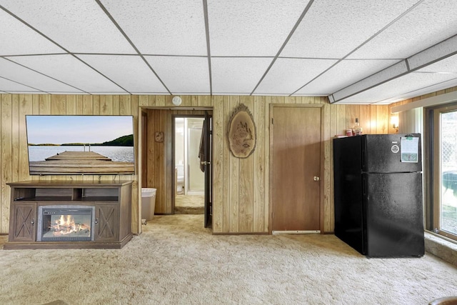 unfurnished living room with light colored carpet, a drop ceiling, and wood walls