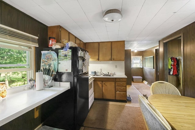 kitchen featuring white range with electric cooktop, sink, black fridge, and wood walls