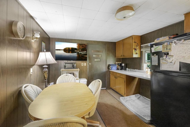 kitchen with black fridge, light carpet, kitchen peninsula, and wood walls