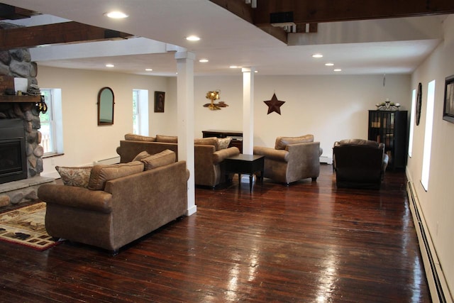 living room featuring dark wood-type flooring, a baseboard heating unit, and a stone fireplace