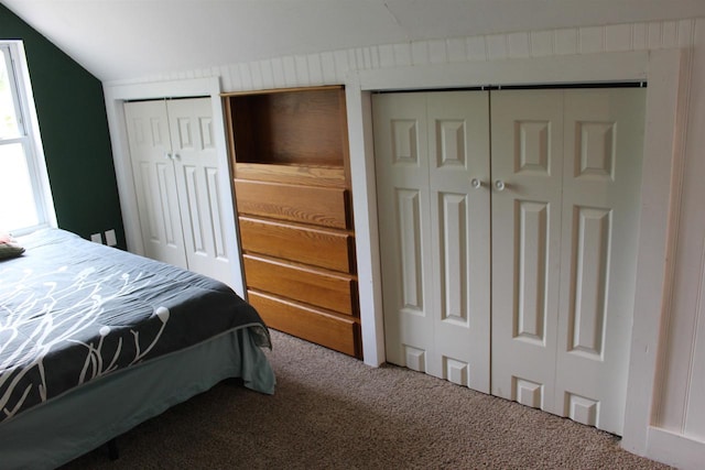 carpeted bedroom with multiple closets and vaulted ceiling