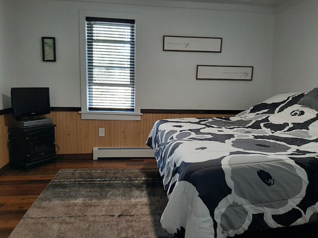 bedroom featuring wood walls, dark wood-type flooring, and a baseboard heating unit