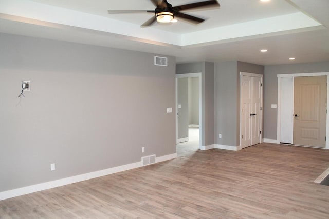 empty room featuring a tray ceiling, ceiling fan, and light hardwood / wood-style flooring