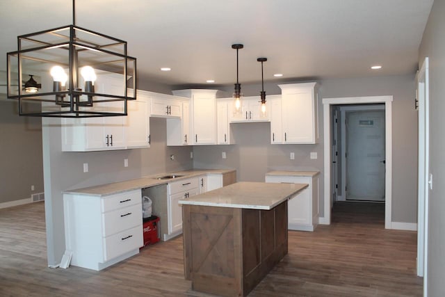 kitchen featuring pendant lighting, white cabinets, a center island, light stone countertops, and dark wood-type flooring