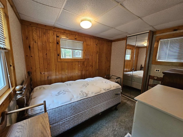 carpeted bedroom with wooden walls, a closet, and a paneled ceiling