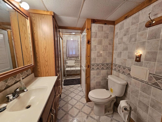 bathroom featuring vanity, toilet, tile walls, and a drop ceiling