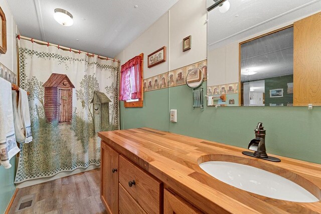 bathroom with walk in shower, wood-type flooring, vanity, and a textured ceiling