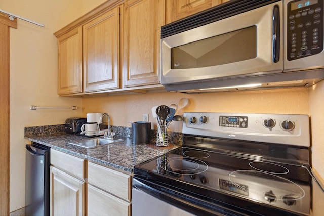 kitchen featuring appliances with stainless steel finishes, sink, light brown cabinetry, and dark stone counters