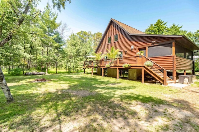 rear view of house featuring a wooden deck, an outdoor fire pit, a yard, and a sunroom