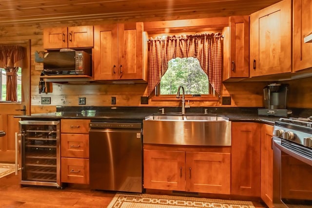 kitchen featuring sink, appliances with stainless steel finishes, wood walls, wine cooler, and light wood-type flooring