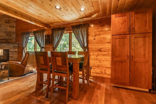 dining space featuring hardwood / wood-style flooring, a stone fireplace, a wealth of natural light, and wooden ceiling