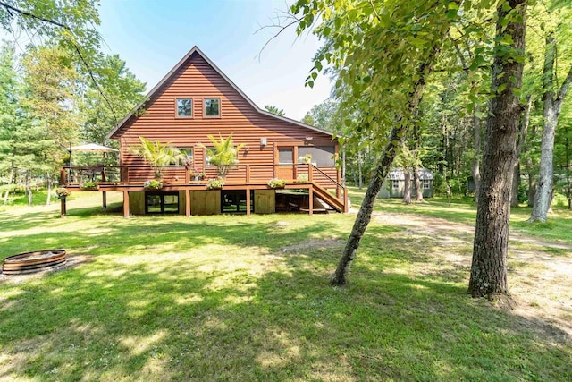 rear view of house featuring a wooden deck, an outdoor fire pit, and a lawn