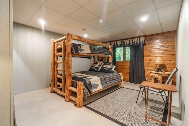 bedroom featuring a paneled ceiling and wooden walls