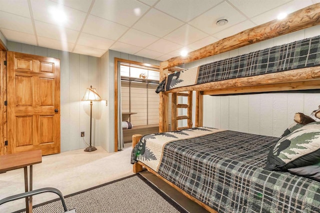 carpeted bedroom featuring a paneled ceiling and wood walls