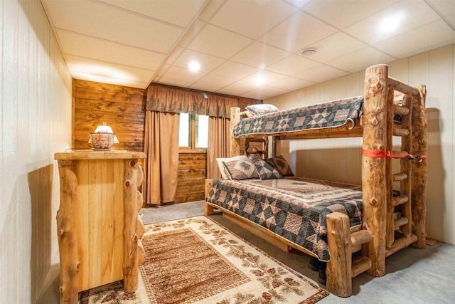 carpeted bedroom featuring a paneled ceiling and wood walls