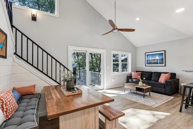living area with wood finished floors, high vaulted ceiling, a ceiling fan, and stairs