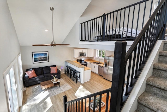 living room with light wood-style floors, high vaulted ceiling, a ceiling fan, and stairs