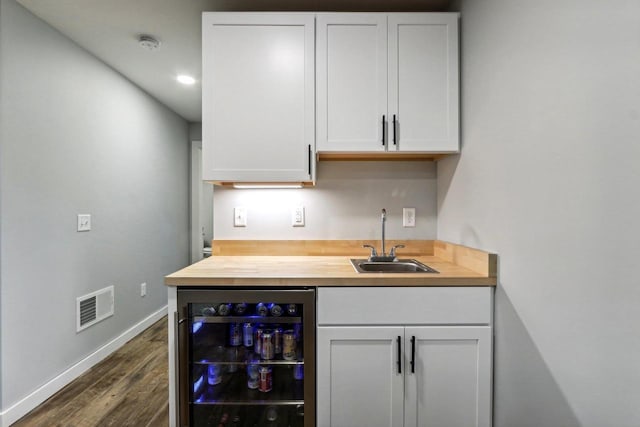bar featuring wet bar, visible vents, a sink, beverage cooler, and dark wood-style floors
