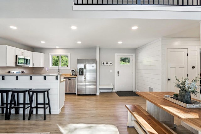 kitchen with light wood-style floors, a kitchen bar, recessed lighting, white cabinetry, and stainless steel appliances