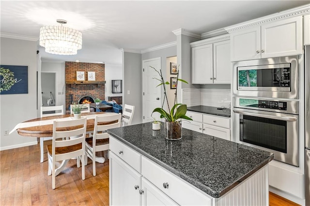 kitchen with decorative light fixtures, a brick fireplace, a kitchen island, white cabinetry, and stainless steel appliances