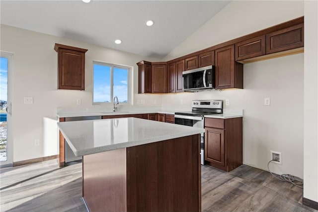 kitchen with a center island, light stone counters, hardwood / wood-style floors, vaulted ceiling, and appliances with stainless steel finishes