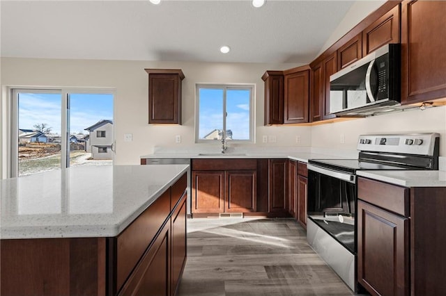 kitchen with a wealth of natural light, sink, stainless steel appliances, light stone counters, and light hardwood / wood-style floors