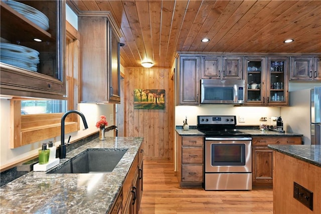 kitchen featuring sink, light wood-type flooring, wooden ceiling, appliances with stainless steel finishes, and dark stone counters