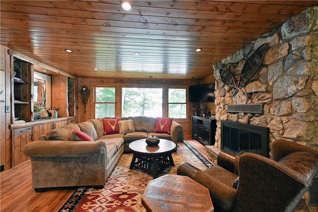 living room featuring wood ceiling, wood walls, a stone fireplace, and light wood-type flooring