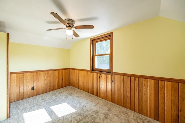 spare room with wooden walls, carpet, ceiling fan, and lofted ceiling