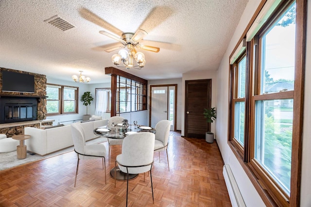 dining space featuring plenty of natural light, parquet floors, a textured ceiling, and a stone fireplace