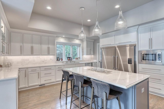 kitchen featuring sink, white cabinetry, built in appliances, a kitchen island, and pendant lighting