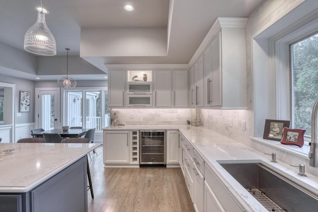 kitchen featuring hanging light fixtures, beverage cooler, white cabinets, and light wood-type flooring