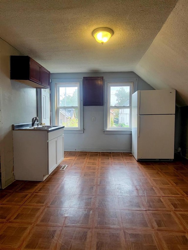 kitchen featuring sink, white cabinetry, white refrigerator, a textured ceiling, and vaulted ceiling