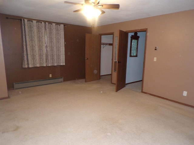 unfurnished bedroom with ceiling fan, baseboard heating, a walk in closet, a closet, and light colored carpet