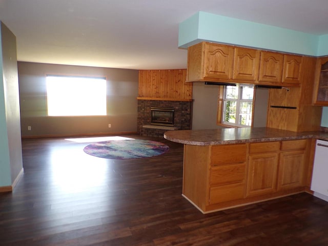 kitchen with kitchen peninsula, dark hardwood / wood-style flooring, and a brick fireplace