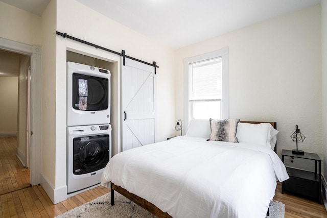 bedroom with light wood-type flooring, a barn door, and stacked washer / dryer