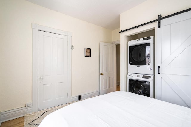 bedroom featuring stacked washer / dryer, a barn door, and hardwood / wood-style floors