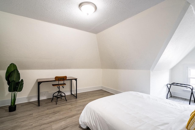 bedroom featuring lofted ceiling, hardwood / wood-style floors, and a textured ceiling