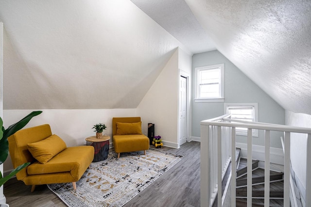 sitting room with lofted ceiling, hardwood / wood-style floors, and a textured ceiling