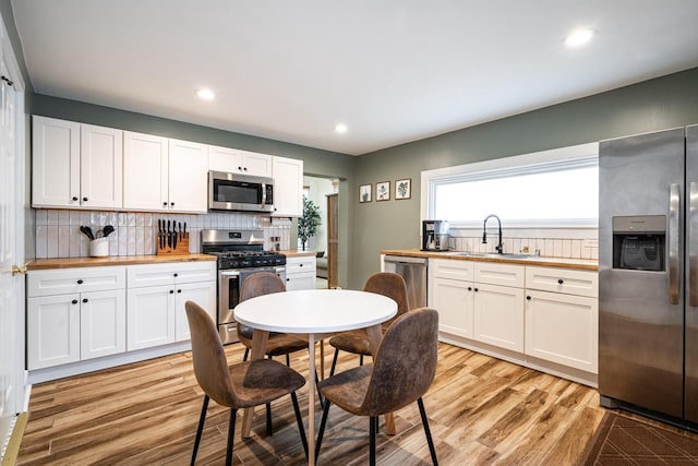 kitchen with sink, appliances with stainless steel finishes, white cabinetry, tasteful backsplash, and light wood-type flooring