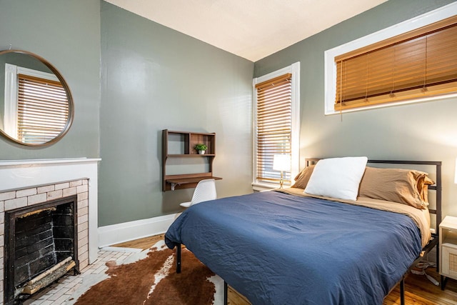 bedroom featuring multiple windows, lofted ceiling, a fireplace, and light hardwood / wood-style flooring