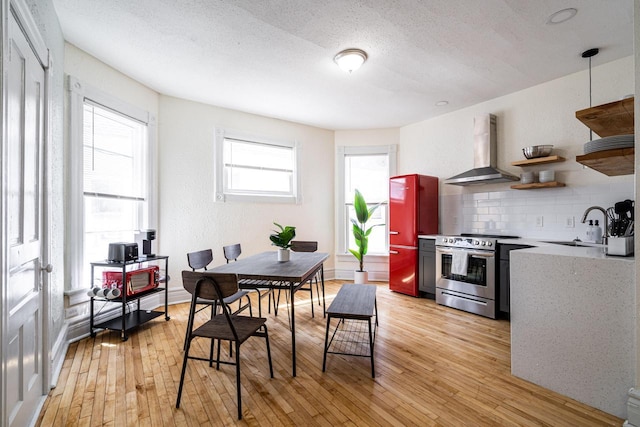 kitchen featuring wall chimney exhaust hood, sink, light wood-type flooring, stainless steel range, and decorative backsplash